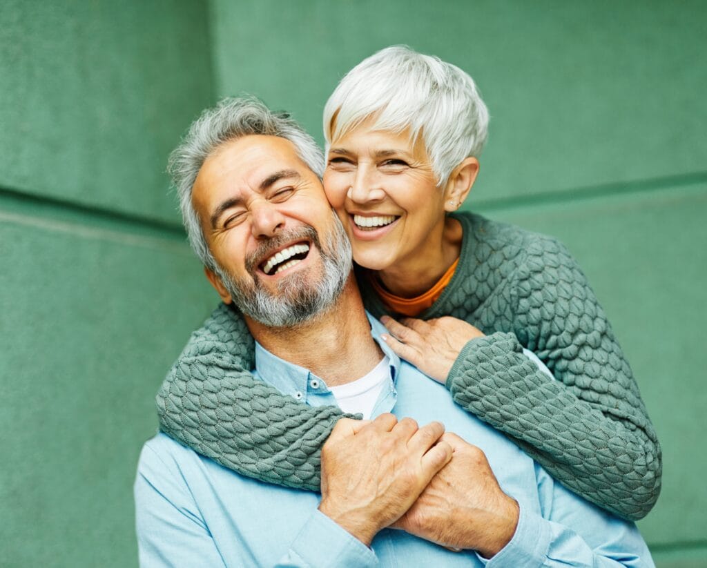 Happy senior couple smiling and embracing outdoors, representing the confidence and joy restored by All-on-4 dental implants.