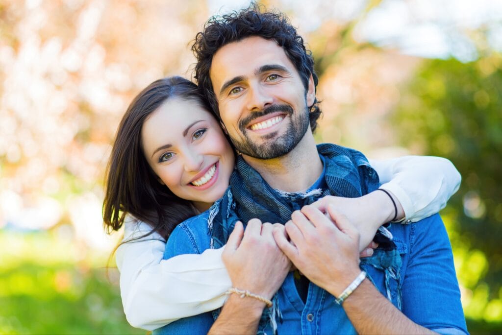 Smiling couple with bright white teeth, showcasing the results of cosmetic dentistry procedures such as teeth whitening or veneers.