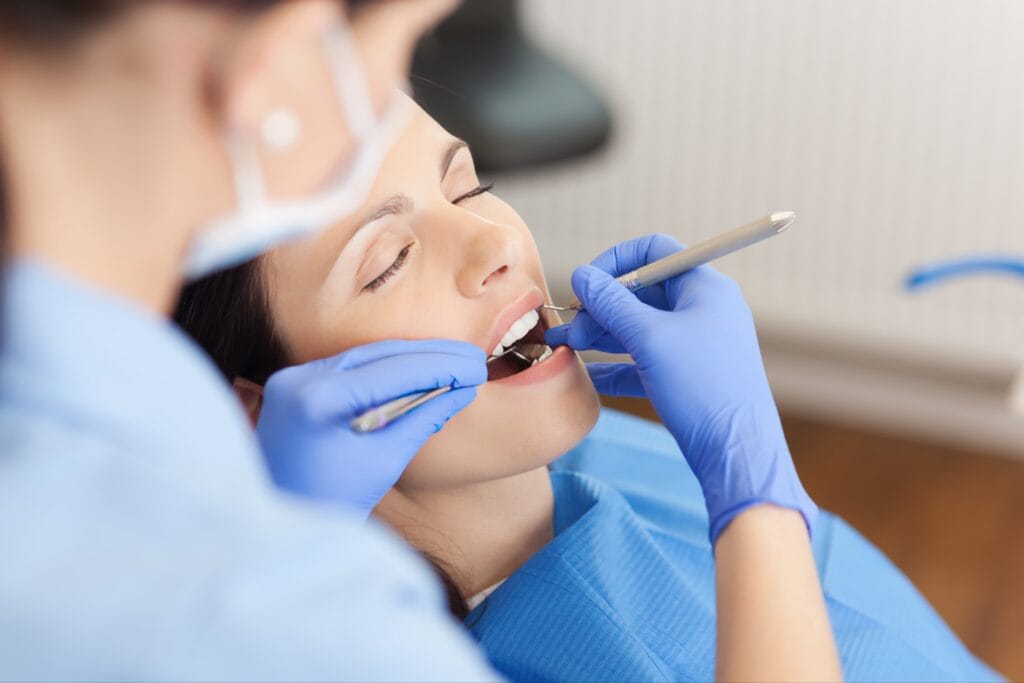 Female patient receiving dental treatment with her eyes closed, while a dental professional uses tools in her mouth—representing sedation dentistry for a relaxed and anxiety-free dental experience.