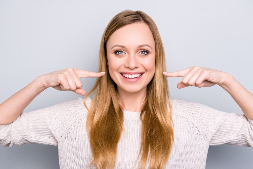 Smiling woman pointing to her bright white teeth, expressing satisfaction—ideal for a dental testimonial or success story.