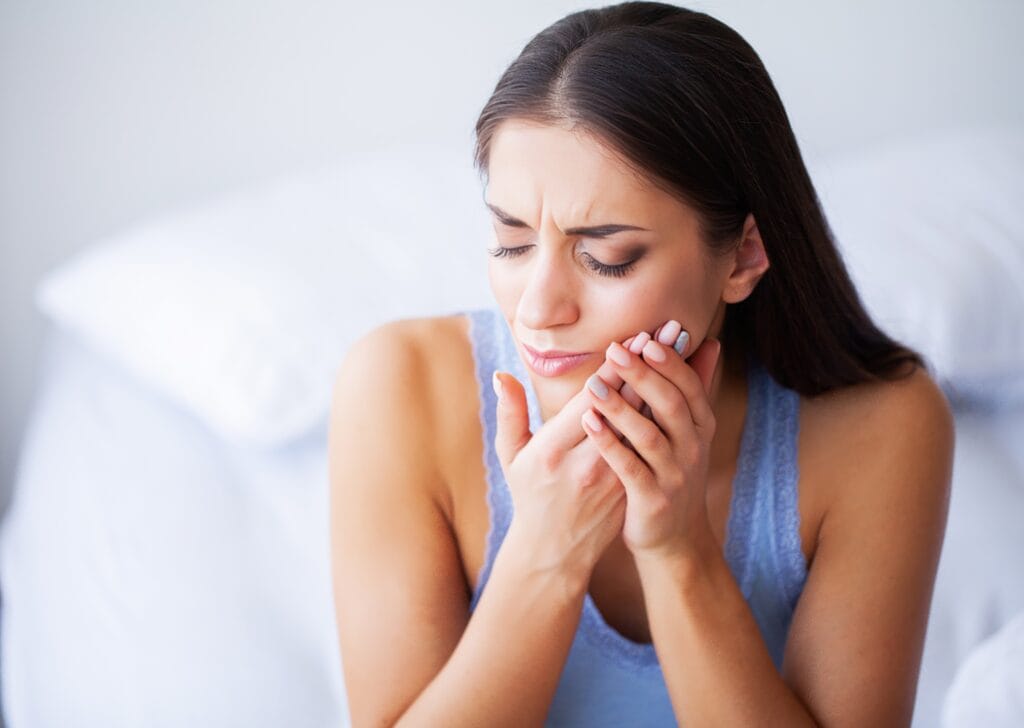 Young woman in pain holding her cheek, indicating a severe toothache or dental discomfort.
